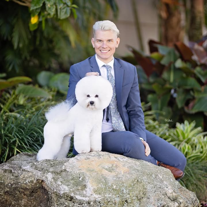 Eric seated in a garden beside a freshly groomed white Bichon Frise
